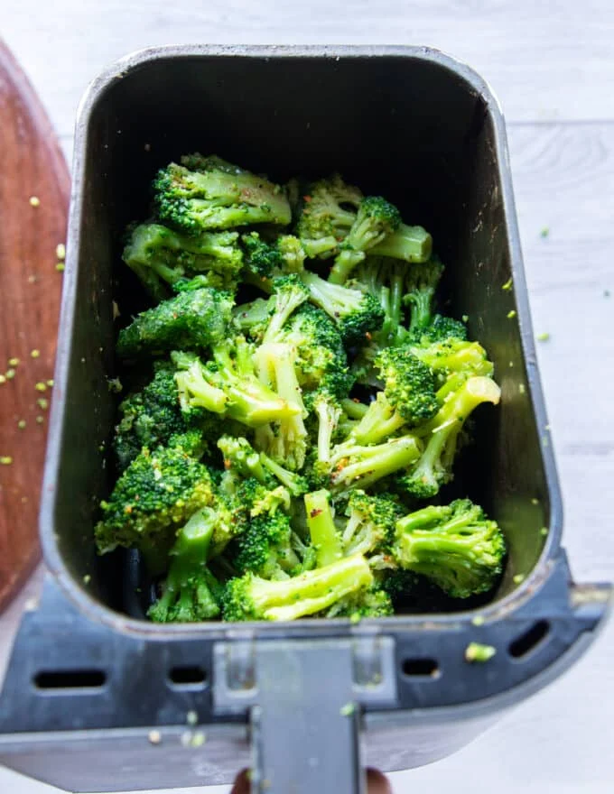 Seasoned frozen broccoli florets in the air fryer basket in a single layer