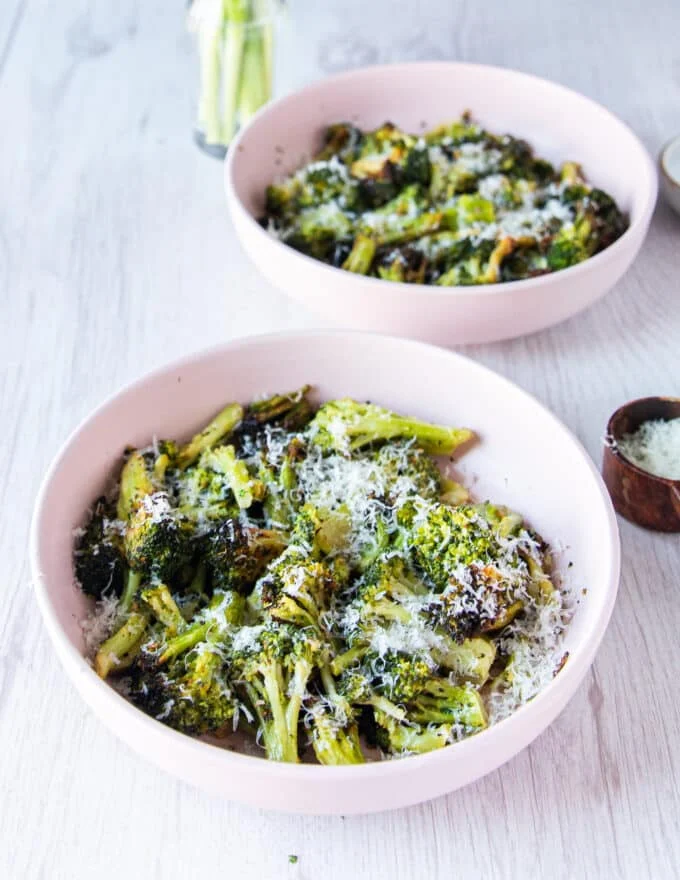 A bowl of frozen broccoli in air fryer ready sprinkled with parmesan cheese