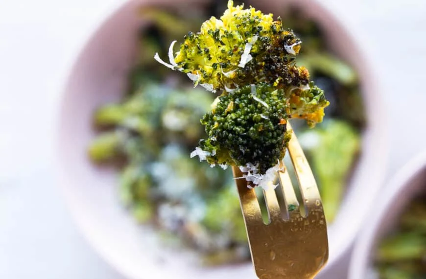 A fork holding an air fryer broccoli piece close up showing the crisp and perfectly cooked broccoli