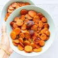 A hand holding a plate of maple glazed carrots with caramelized fork tender carrots