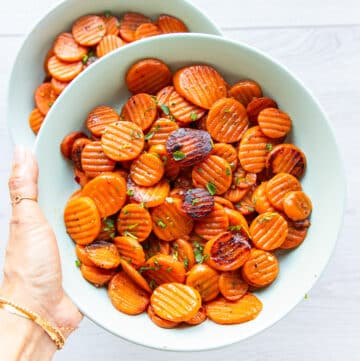 A hand holding a plate of maple glazed carrots with caramelized fork tender carrots