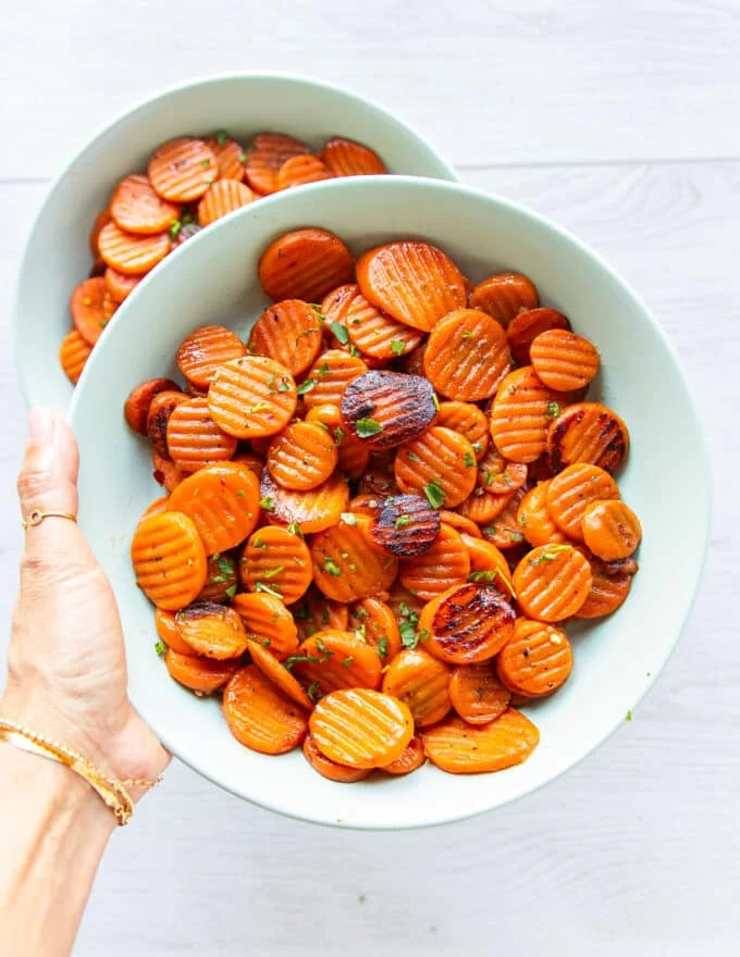 A hand holding a plate of maple glazed carrots with caramelized fork tender carrots