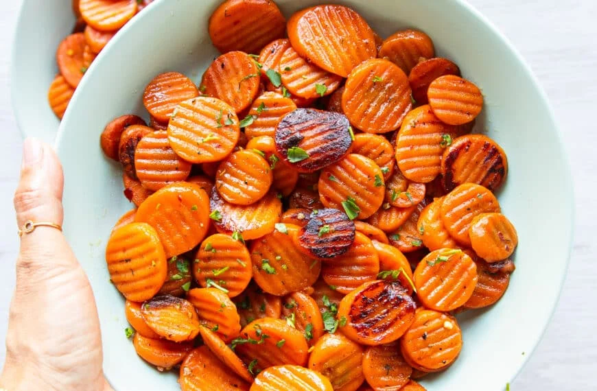 A hand holding a plate of maple glazed carrots with caramelized fork tender carrots