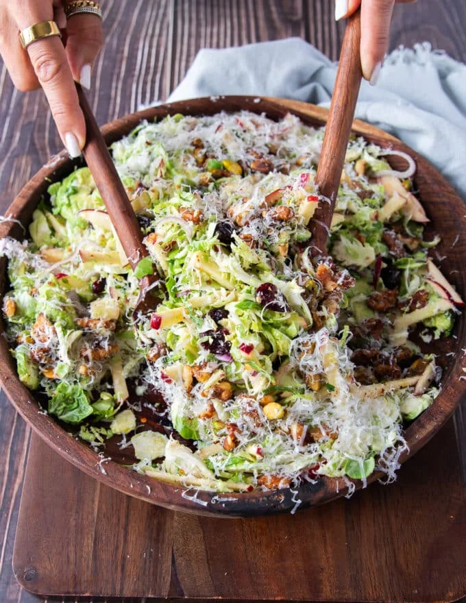 two wooden spoons scooping some Brussel sprout salad with parmesan and walnuts on top