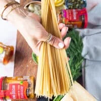 A hand holding long pasta to cook before making the tuna pasta sauce