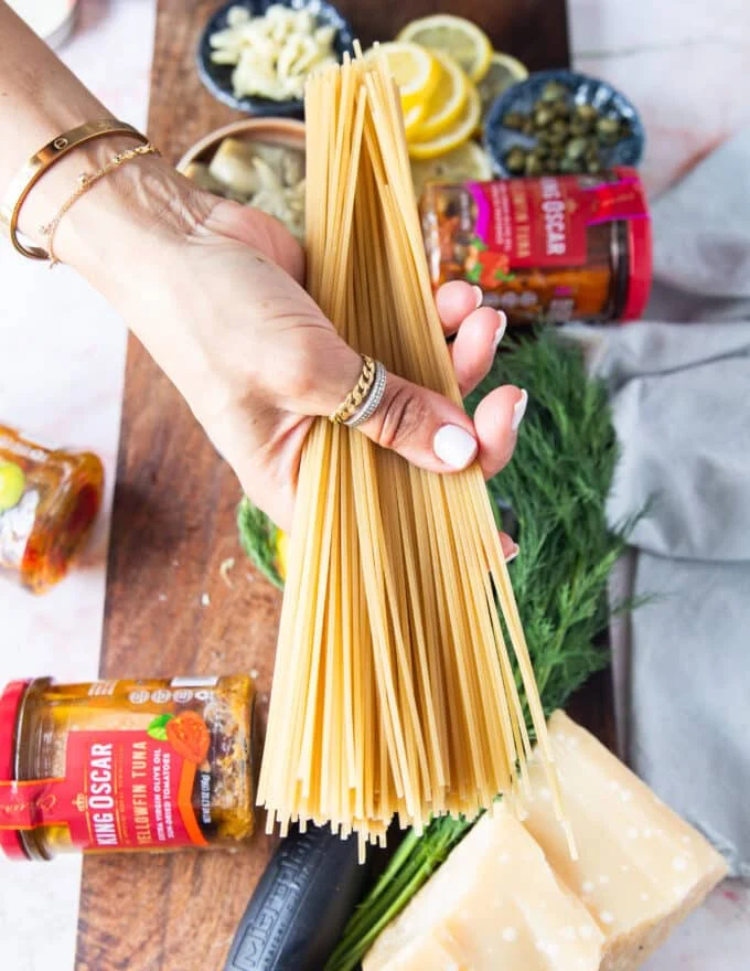 A hand holding long pasta to cook before making the tuna pasta sauce