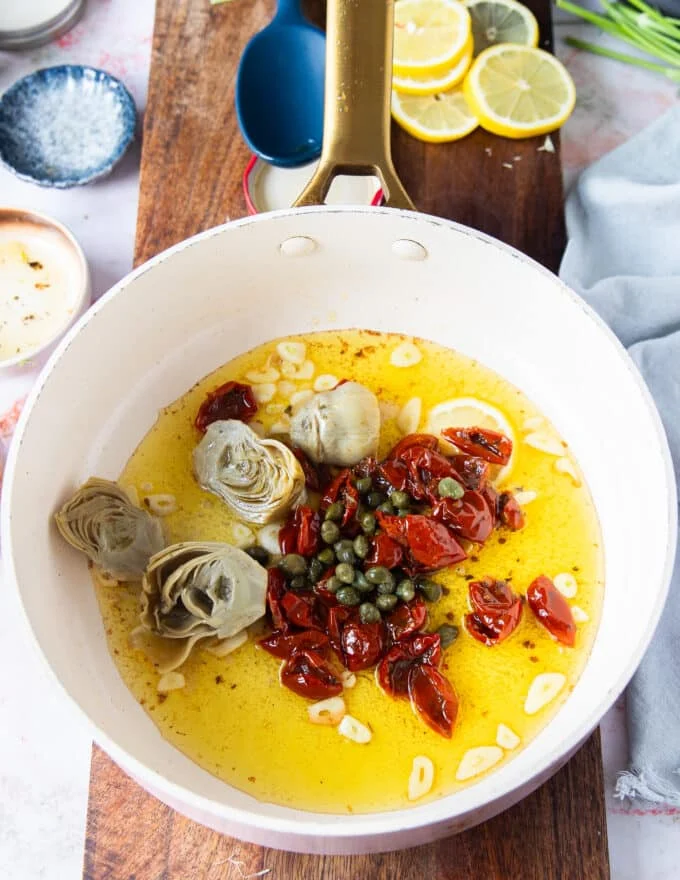 sun dried tomato, capers and artichokes are added to the sliced garlic once it's toasted in the saucepan