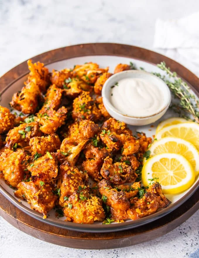 A plate of buffalo cauliflower with lemon slices and ranch bowl for dipping
