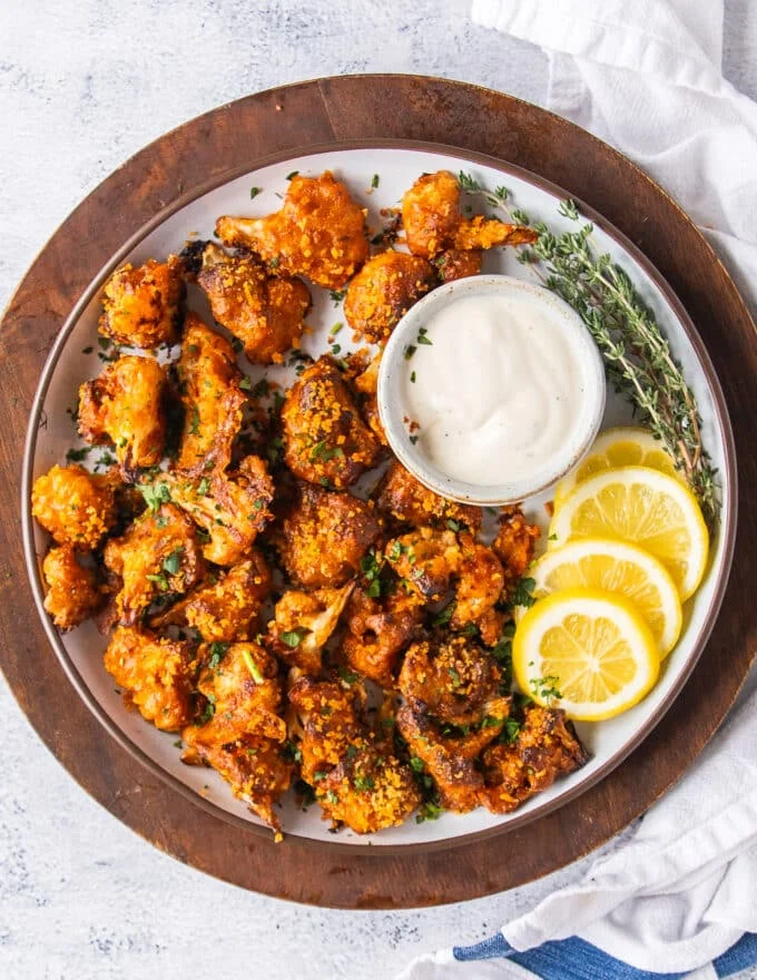 A plate of buffalo cauliflower with lemon slices and a small bowl of ranch dipping sauce