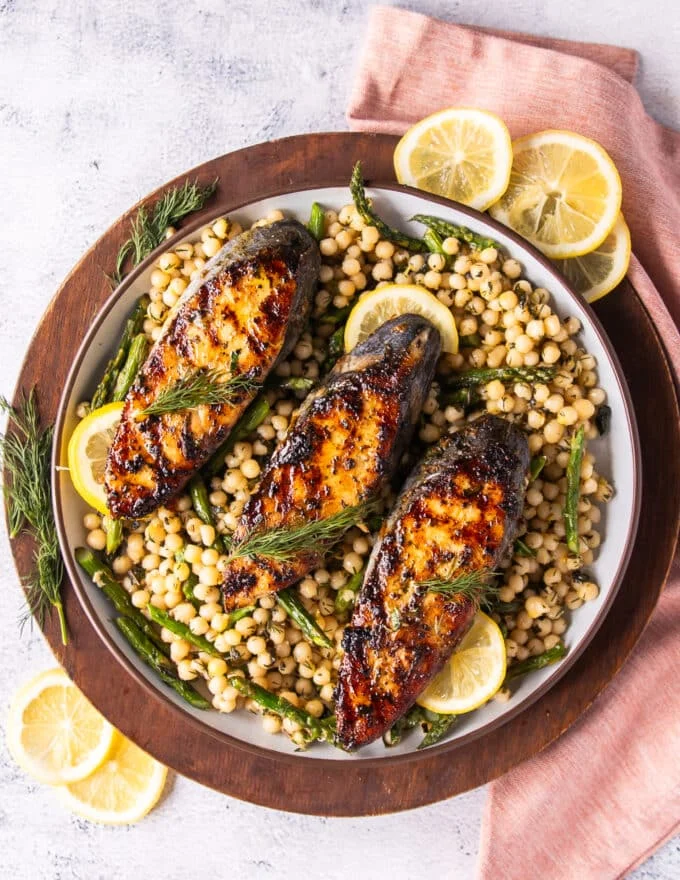 A platter of grilled king mackerel served with lemon wedges, herbs