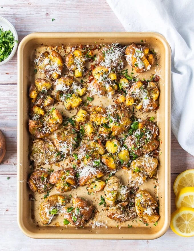 A tray of smashed potatoes finished with parmesan cheese, herbs, and more seasoning