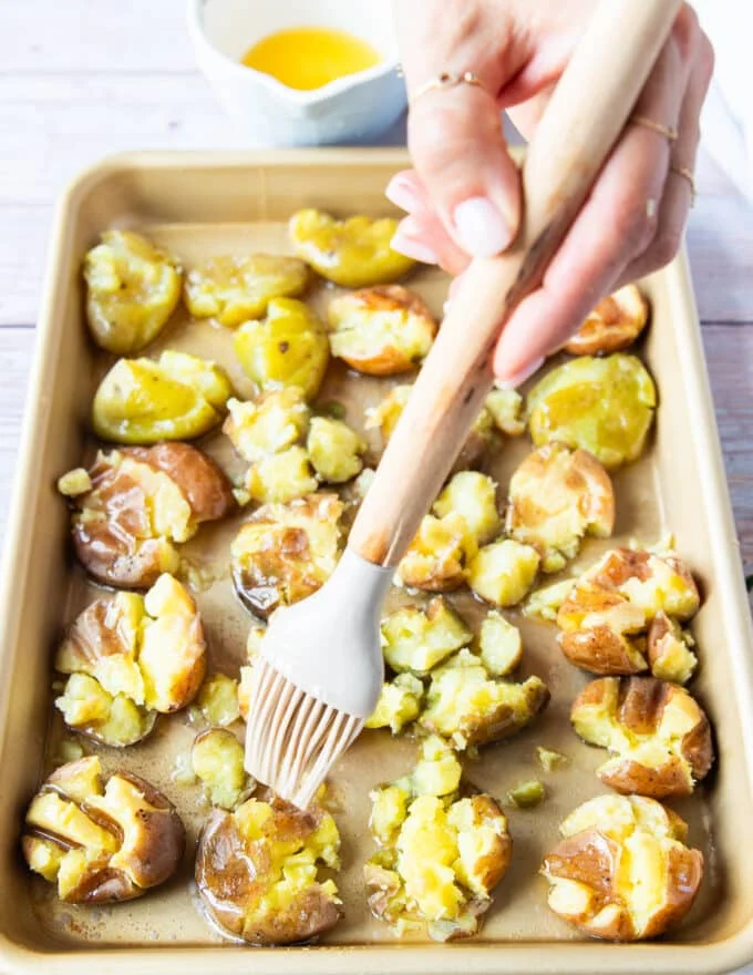 Oil and butter drizzled over a tray of smashed potatoes