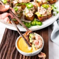 a hand dipping a spicy tuna crispy rice in spicy mayo using chopsticks