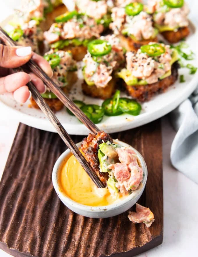a hand dipping a spicy tuna crispy rice in spicy mayo using chopsticks
