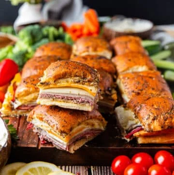 close up of stacked roast beef sliders on a large board with bowls of creamy dips
