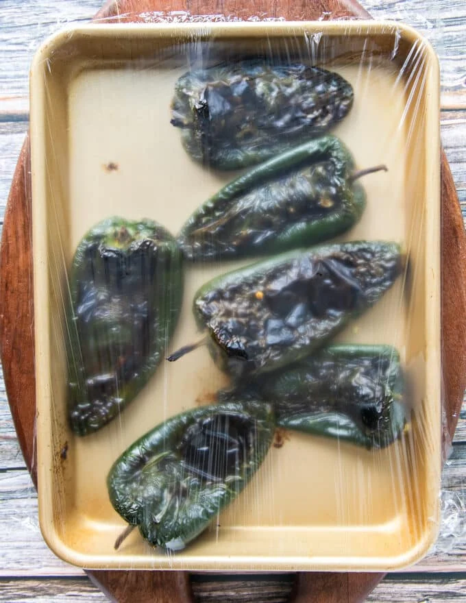 charred peppers covered with plastic wrap to steam