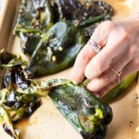 A hand peeling off the skin from the charred peppers
