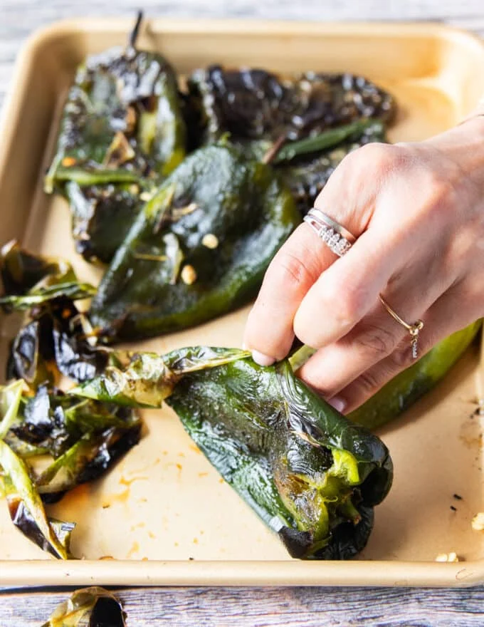 A hand peeling off the skin from the charred peppers