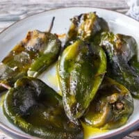 Side view of roasted poblanos on a plate with olive oil and salt
