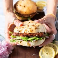 Two hands holding a tuna burger close up showing the layers of avocado, bun, tuna burger, lettuce and other toppings