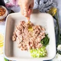A hand mashing the canned tuna into a bowl to make the texture smooth