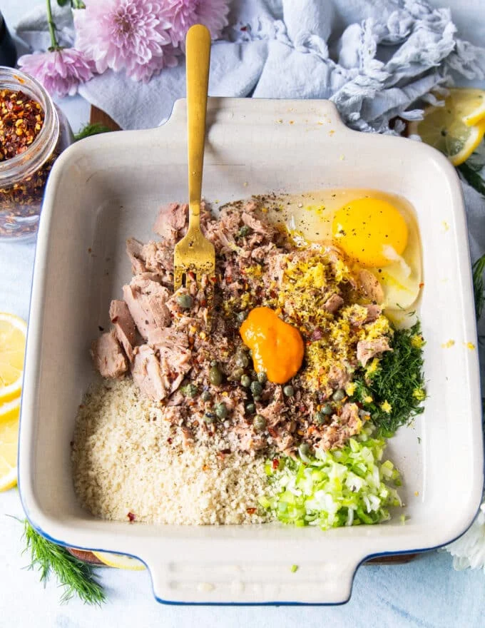 All the tuna burger patty recipe ingredients are added to a bowl such as egg, panko, mustard, herbs, green onions and more