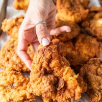 a hand holding on of the deep fried crunchy spicy chicken on a large plater