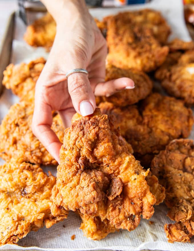 a hand holding on of the deep fried crunchy spicy chicken on a large plater