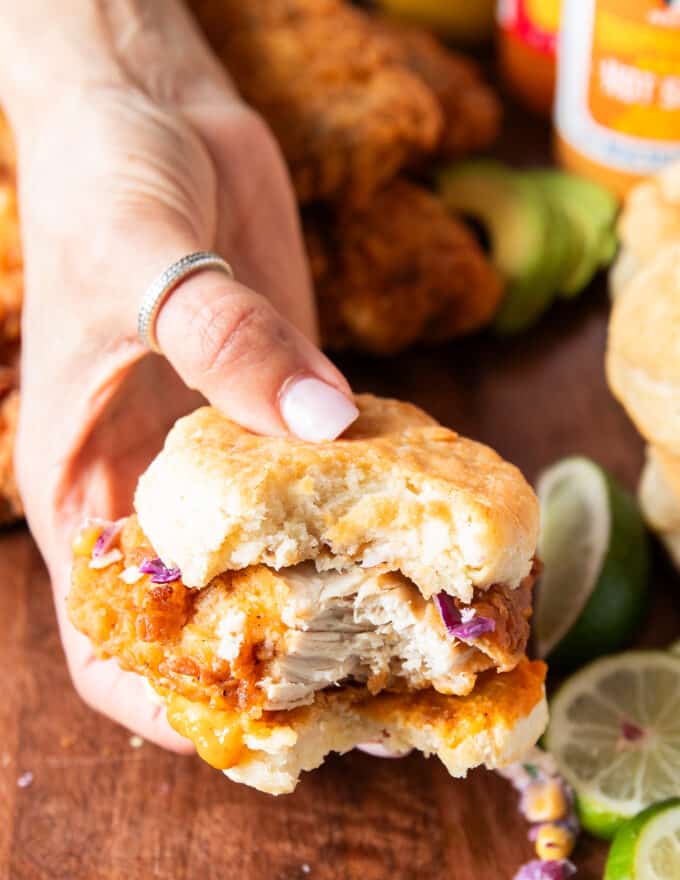 A bitten piece of chicken biscuit showing the juicy and crispy chicken and the buttery biscuit