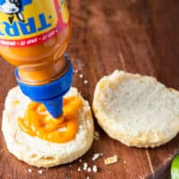 A hand spreading hot sauce over a biscuit