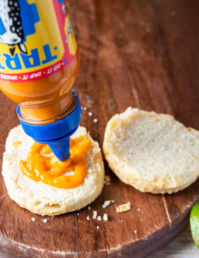 assembling the chicken biscuit by splitting the biscuit in half and spreading the sauce at the bottom