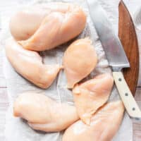 The chicken is sliced into half on a board to prepare for breading