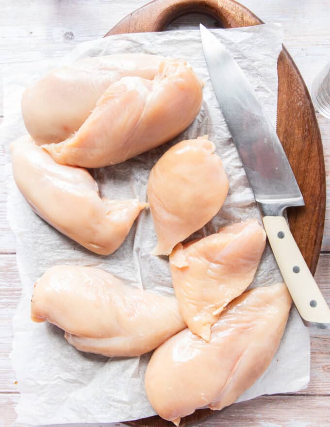 The chicken is sliced into half on a board to prepare for breading