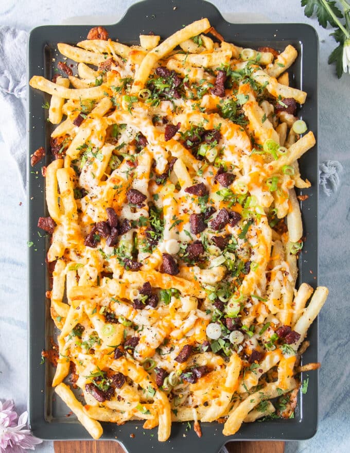 A large tray of loaded fries with cheese, bacon, green onions, sauce and herbs