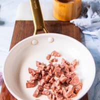 The bacon or sausage added to a skillet over high heat and ready to crisp up