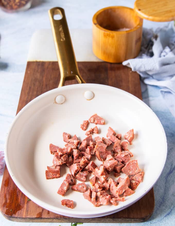 The bacon or sausage added to a skillet over high heat and ready to crisp up