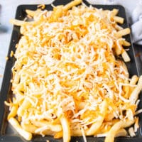 A layer of cheese is added over the cooked fries on a baking sheet and ready to go into the oven