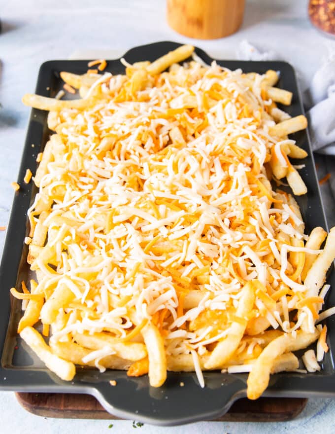 A layer of cheese is added over the cooked fries on a baking sheet and ready to go into the oven