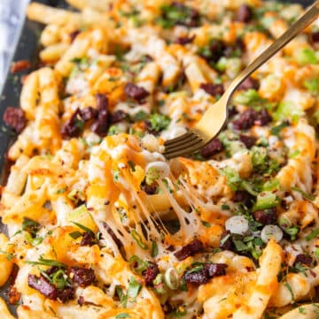 A fork pulling some cheese fries showing the cheese pull and all the toppings on top