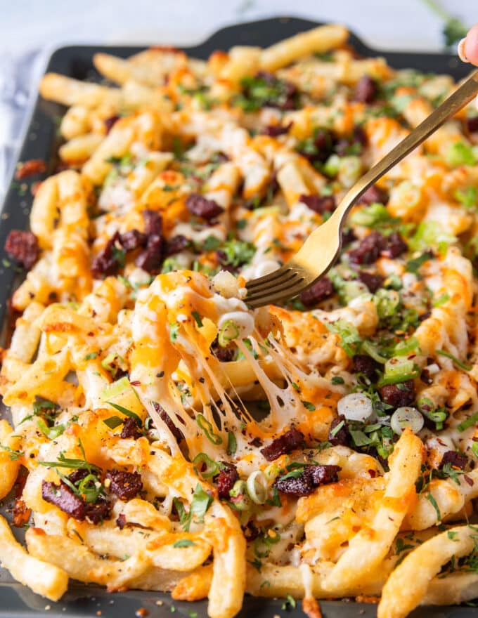 A fork pulling some cheese fries showing the cheese pull and all the toppings on top