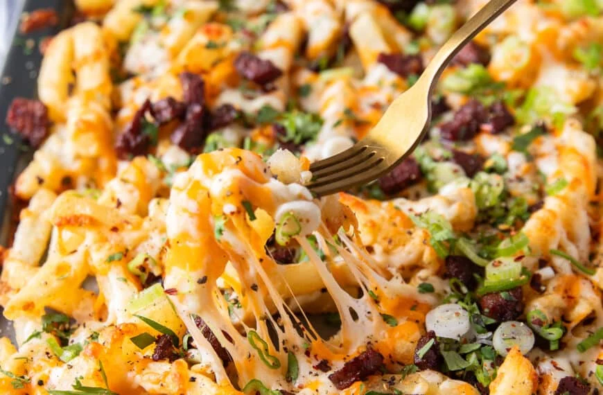 A fork pulling some cheese fries showing the cheese pull and all the toppings on top