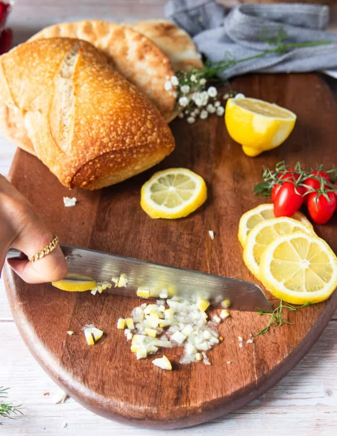 A hand slicing lemon slices into pieces for a secret ingredient to the sandwich by infusing maximum lemon flavor