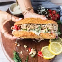two hands holding a finished sardine sandwich fully assembled and ready to enjoy showing the layers
