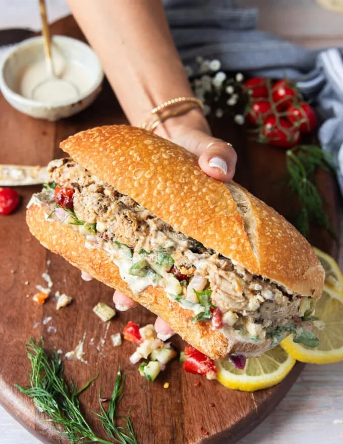 A hand holding a sardine sandwich fully loaded and layered