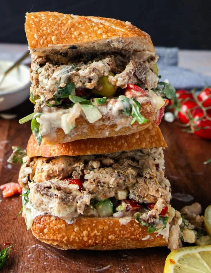 Cut up sardine sandwich in half close up shwoing the layers of sardines and fresh ingredients stuffed inside the sandwich bread