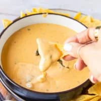 A hand holding a chip dipping the chips in the smoked queso