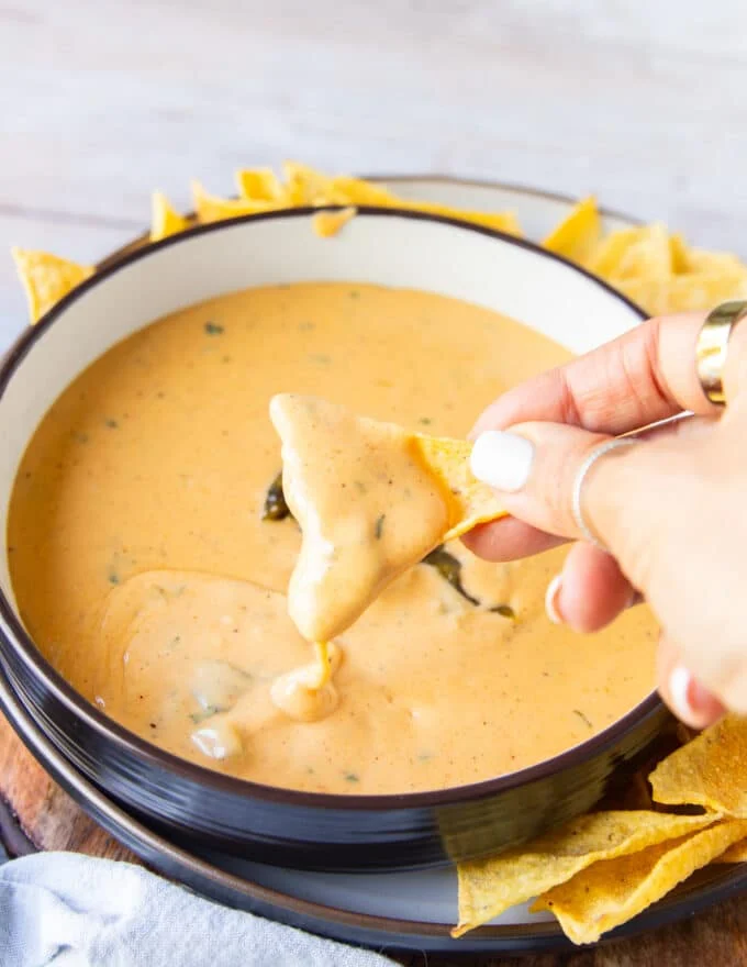 A hand holding a chip dipping the chips in the smoked queso