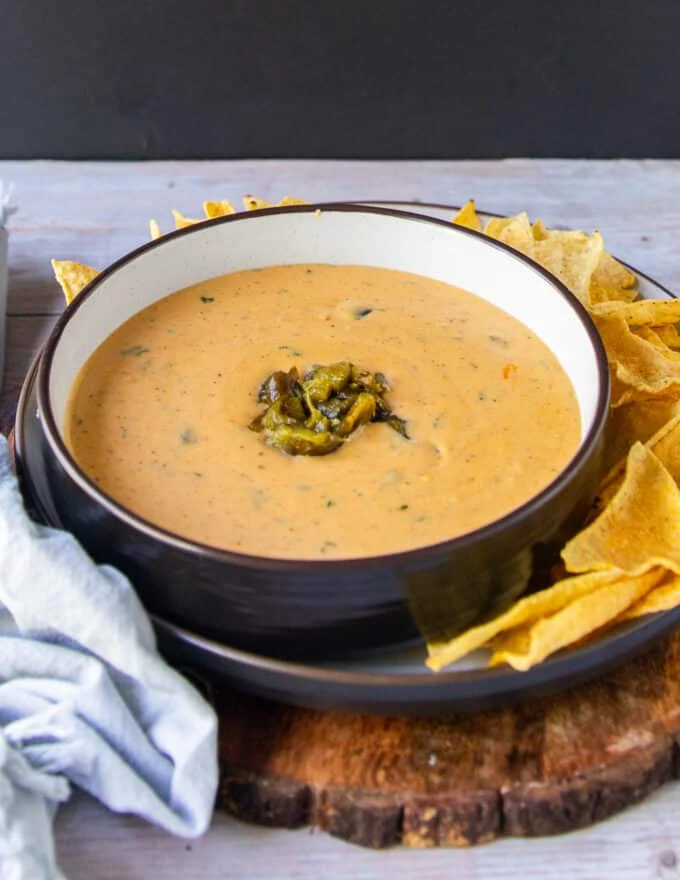 side view of a bowl of smoky queso with roasted poblanos and chips for serving