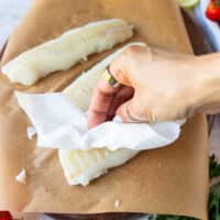 A hand patting the cod fish dry using paper towels
