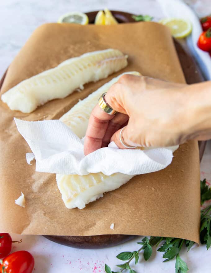 A hand patting the cod fish dry using paper towels
